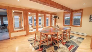Un espace repas avec une table et des chaises en bois, de grandes fenêtres et une vue sur l’extérieur.