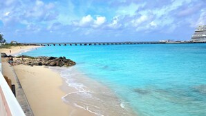 Una spiaggia con acque turchesi cristalline, un molo che si protende sull'oceano e una nave da crociera ormeggiata nelle vicinanze.