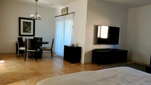 Una camera d'albergo con un letto, una televisione, una scrivania con sedie, un lampadario e una finestra con tende.