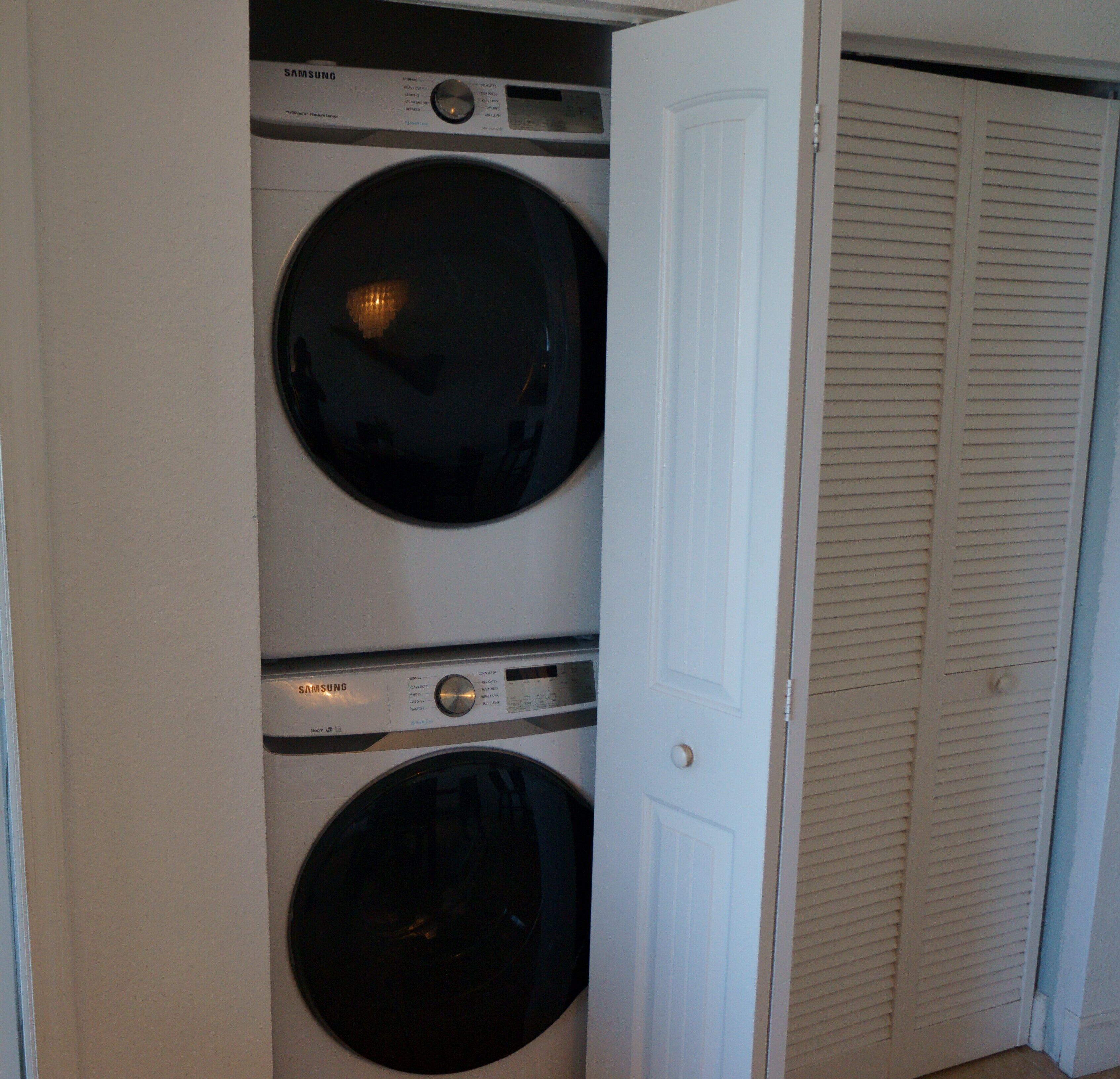 Une buanderie équipée de deux machines à laver et deux sèche-linge superposés, une porte donnant sur un placard et un mur blanc.