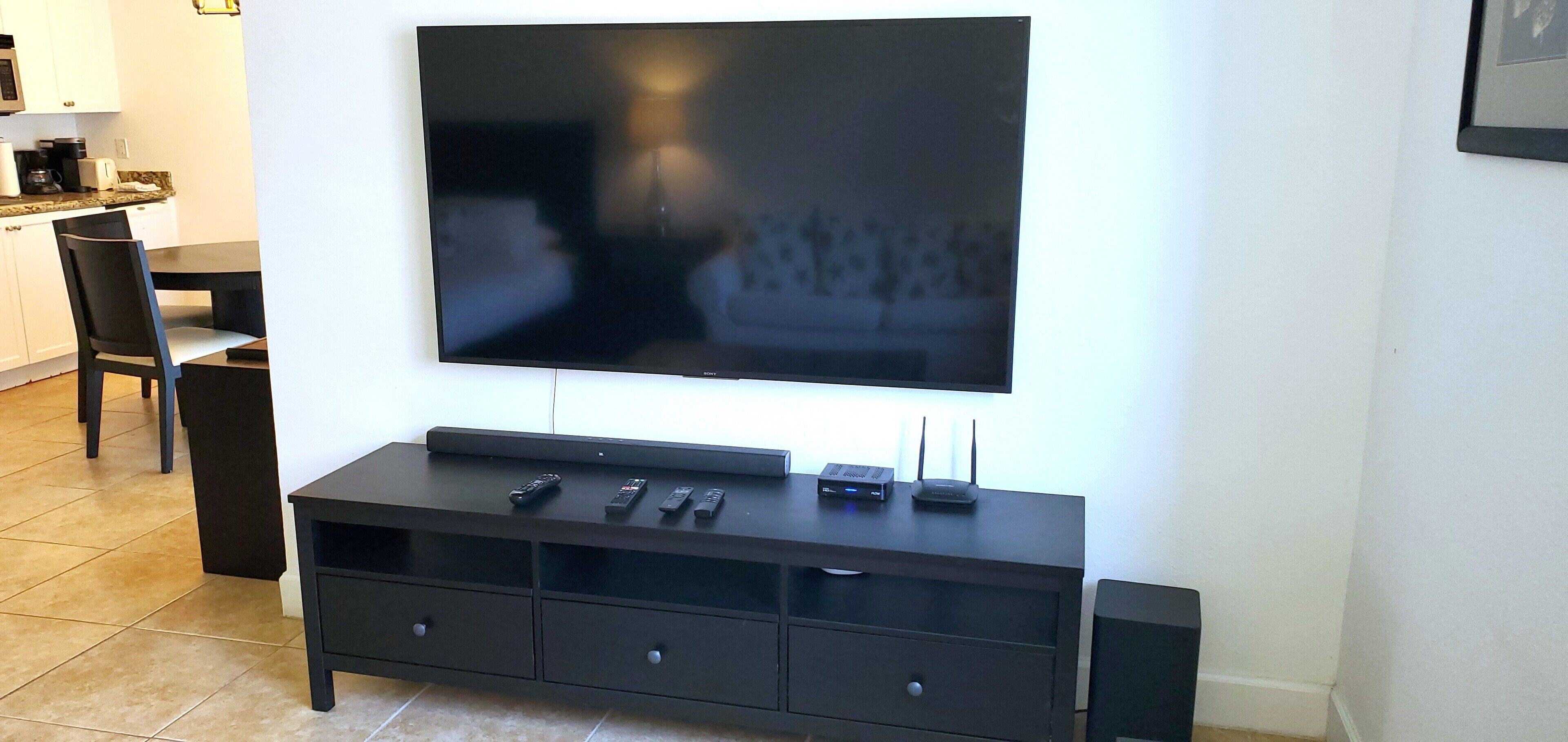 A flat-screen TV mounted on a wall above a dark wooden entertainment center with remote controls and a router.