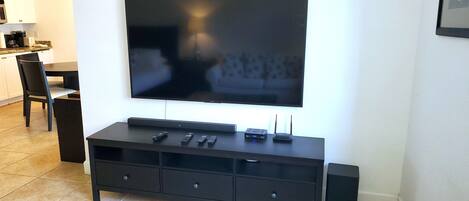 A flat-screen TV mounted on a wall above a dark wooden entertainment center with remote controls and a router.