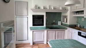 Een keuken met witte kastjes, een groene betegelde achterwand, een inbouwoven en een hanglamp.