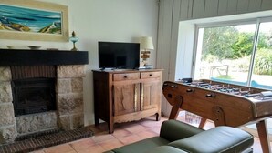 Een woonkamer met een open haard, een televisie, een tafelvoetbaltafel en een bank.