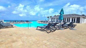 A pool area with lounge chairs and umbrellas, a clear view of the ocean, and a building with large windows. - "Beachside Retreat" 2 Bedroom / 2 Bath (Bimini, Bahamas)