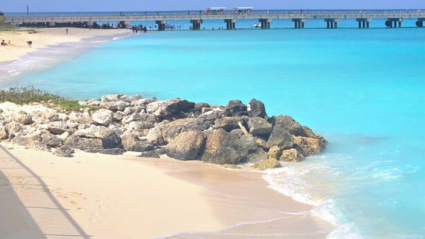 A beach with clear turquoise water, a rocky outcrop, and a pier extending into the sea. - "Beachside Retreat" 2 Bedroom / 2 Bath (Bimini, Bahamas)