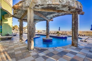 A pool area with a wooden structure overhead, lounge chairs, and a clear view of the ocean. - Towers On The Grove Condo (North Myrtle Beach)