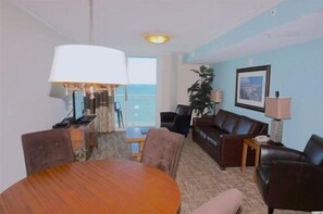 A hotel room with a dining table, two sofas, a TV, and a balcony with a view. - Towers On The Grove Condo (North Myrtle Beach)