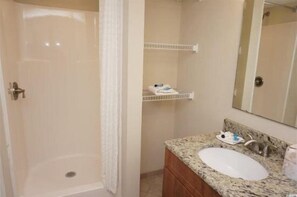 A bathroom with a shower, a sink with a granite countertop, and a mirror above the sink. - Towers On The Grove Condo (North Myrtle Beach)