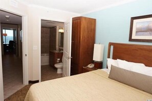 A hotel room with a bed, a wooden wardrobe, a bedside table with a lamp, and a bathroom visible through an open door. - Towers On The Grove Condo (North Myrtle Beach)