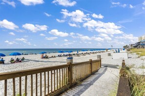 A beach with a wooden boardwalk leading to the shore, umbrellas, and beach chairs. - The Summit 1222 (Panama City Beach)