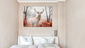 Une chambre à coucher avec un grand lit, du linge de lit blanc et un tableau représentant un cerf dans une forêt.