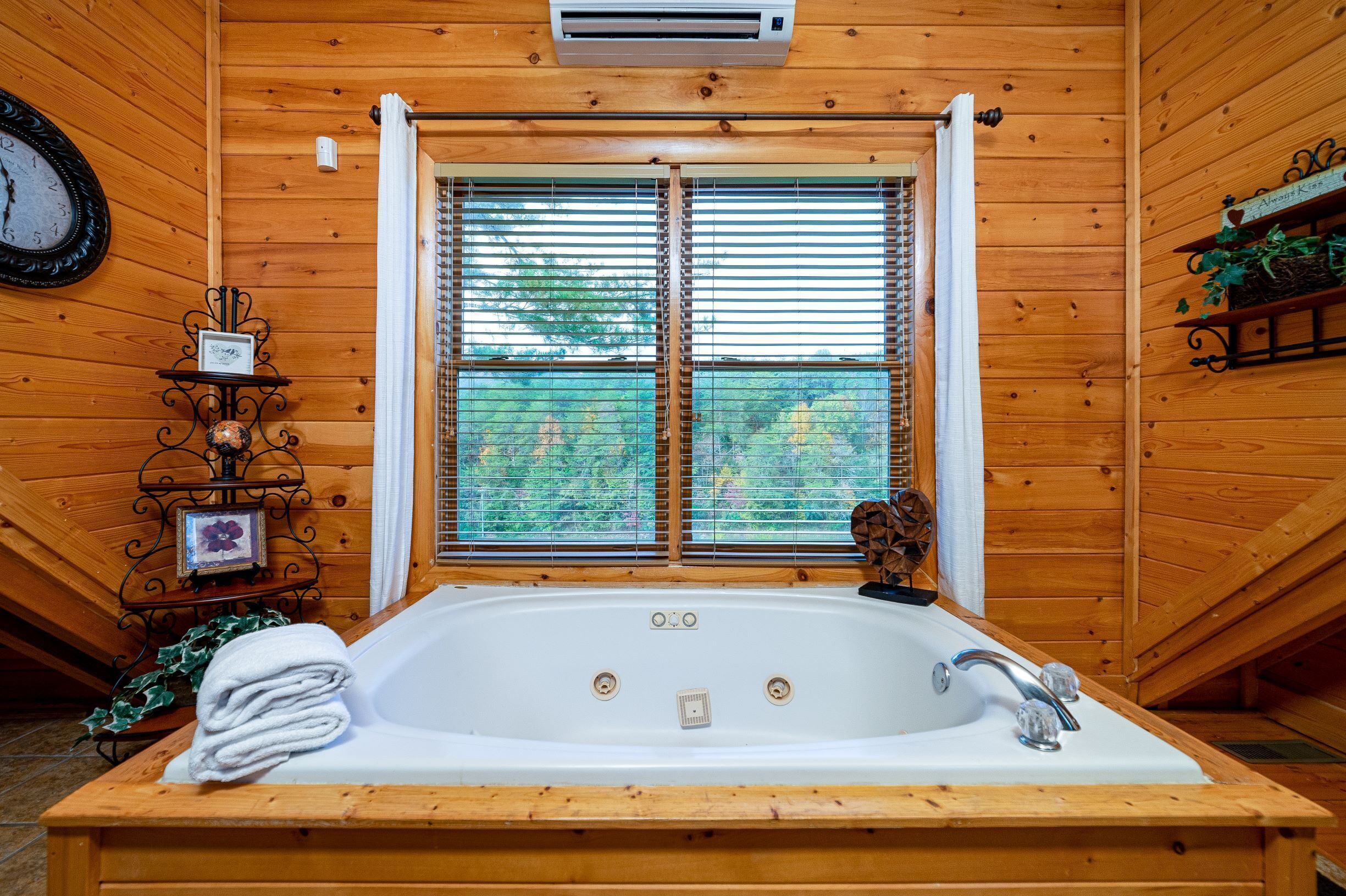 A wooden cabin with a large bathtub, a clock, and a window with blinds.