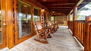 Une véranda en bois avec des fauteuils à bascule, des balustrades en bois et de grandes fenêtres.
