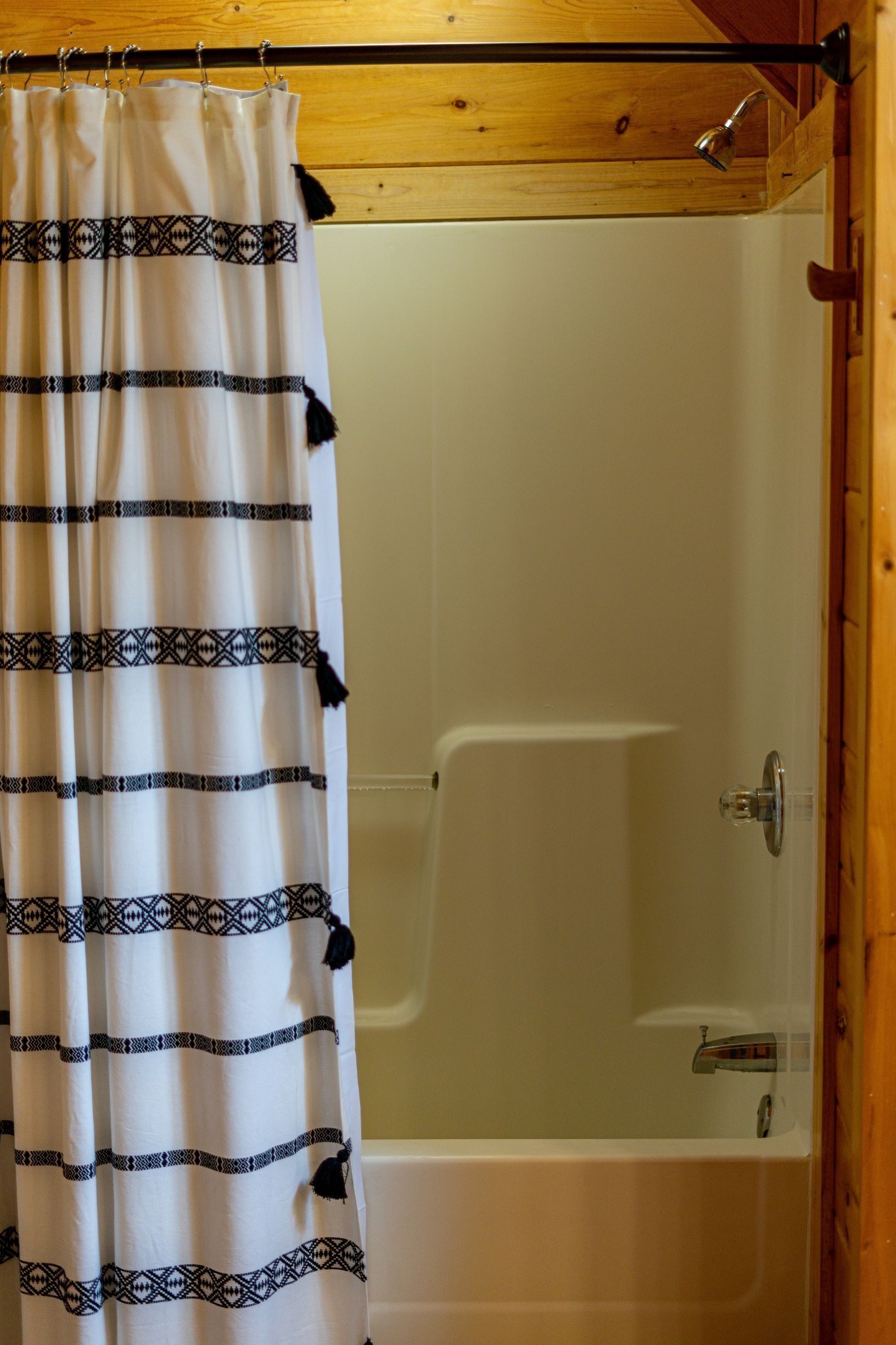 Cabina doccia con tenda bianca decorata con motivi geometrici neri e frange.