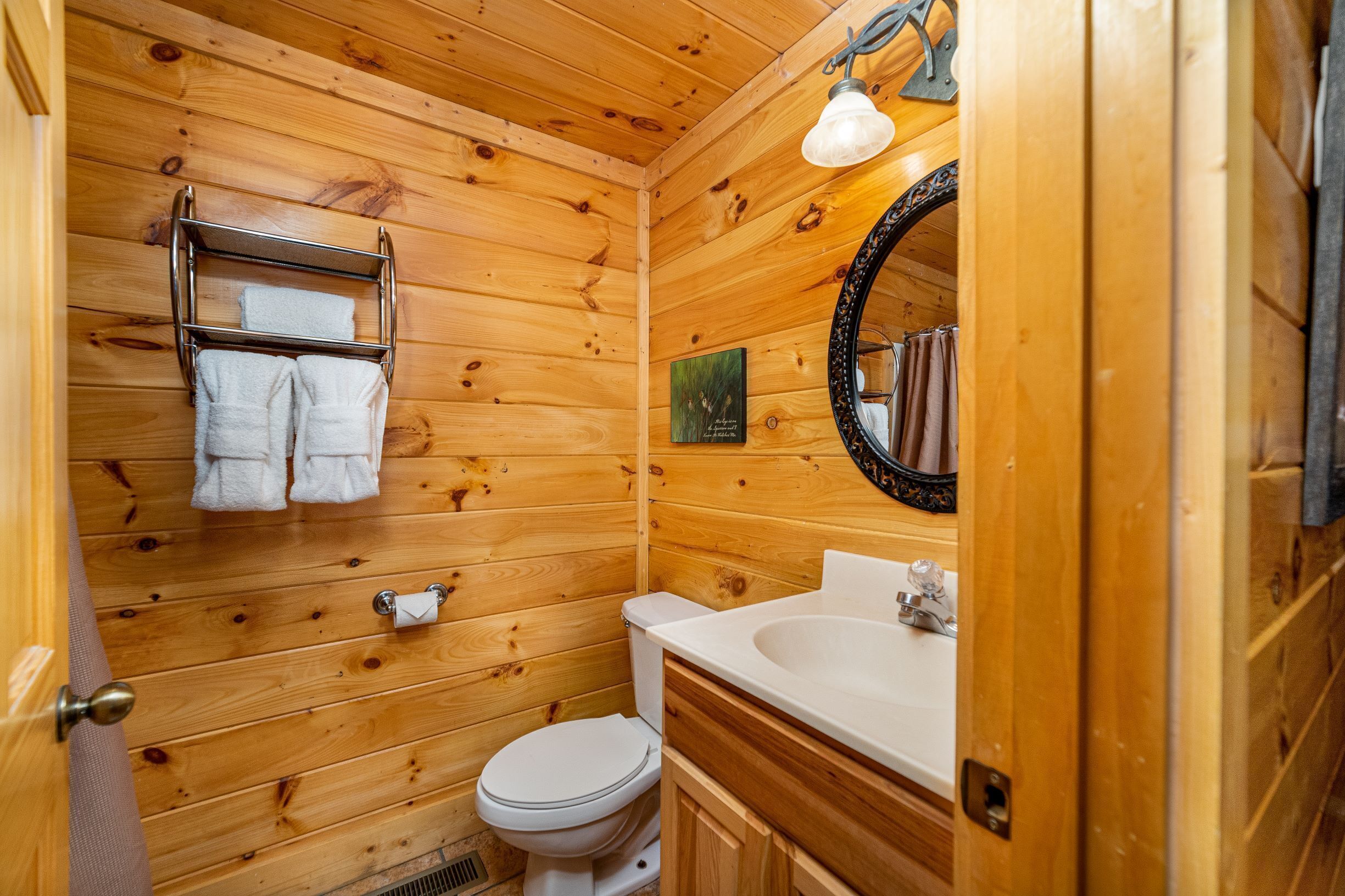 A wooden cabin bathroom with a toilet, sink, and towel rack.
