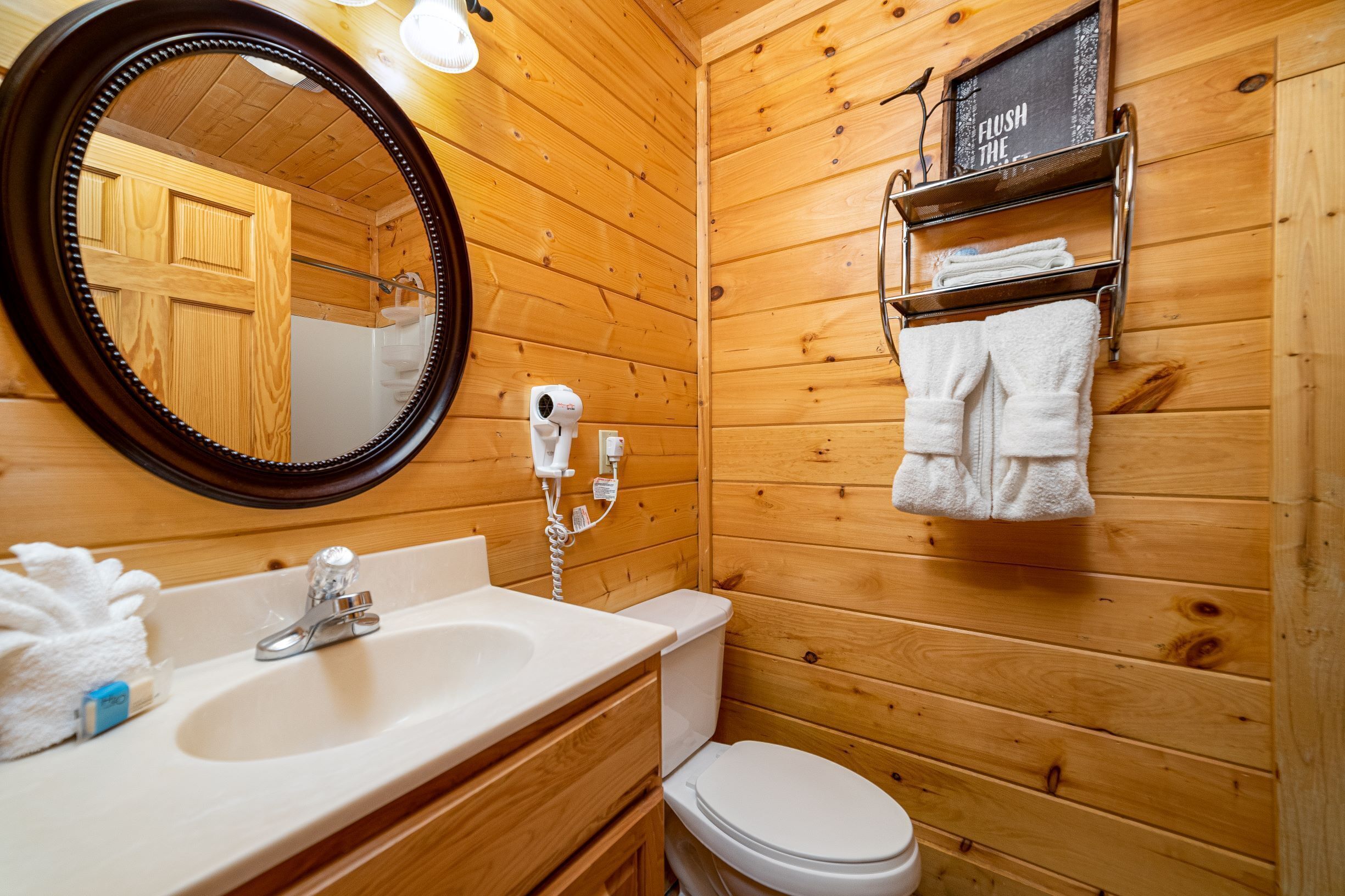 Une salle de bain rustique, aménagée dans une cabane en bois, comprenant un lavabo, des toilettes, un miroir et un porte-serviettes.