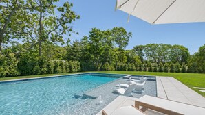 Una piscina con agua cristalina, rodeada de césped cuidado y árboles.