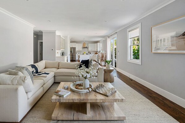 A modern living room with a sectional sofa, a coffee table with decorative items, and a kitchen in the background.
