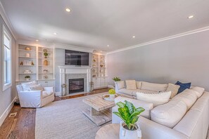 A living room with a fireplace, white sofas, a coffee table, and a bookshelf.