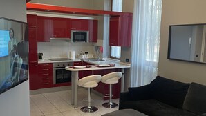 Una cocina moderna con armarios rojos, una isla central con taburetes, una mesa de comedor y un sofá negro en la zona de estar.