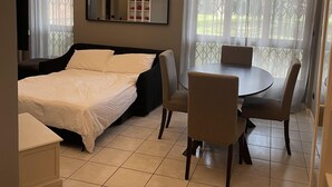 Habitación de hotel con cama, mesa de comedor con sillas, televisión y ventana con cortinas.