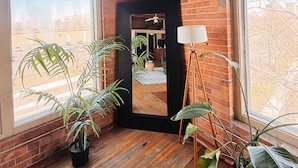 A room with brick walls, wooden flooring, a large mirror, and potted plants. - 420 Friendly Loft • Downtown Detroit Views, Walk to Riverfront, Free Parking (Detroit)
