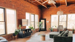 A spacious room with a wooden ceiling, large windows, a bed, a green sofa, and a coffee table. - 420 Friendly Loft • Downtown Detroit Views, Walk to Riverfront, Free Parking (Detroit)