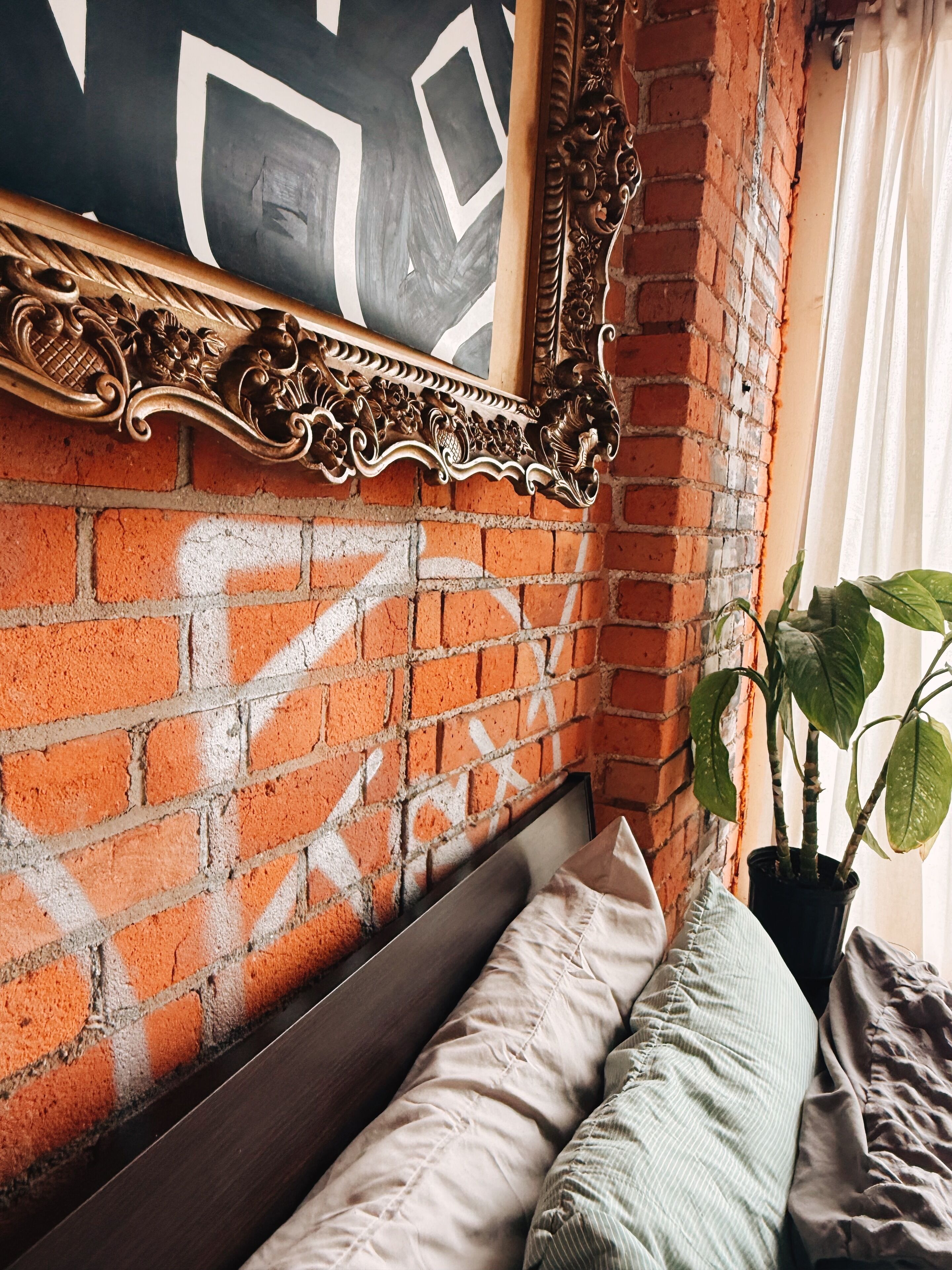 Pared de tijolos com moldura decorativa, um travesseiro e um vaso de planta.