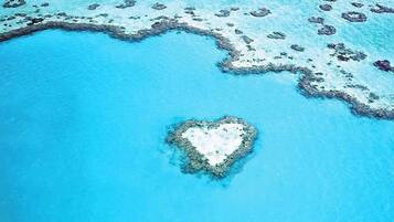 An aerial view of a heart-shaped island surrounded by clear blue waters and scattered coral formations.