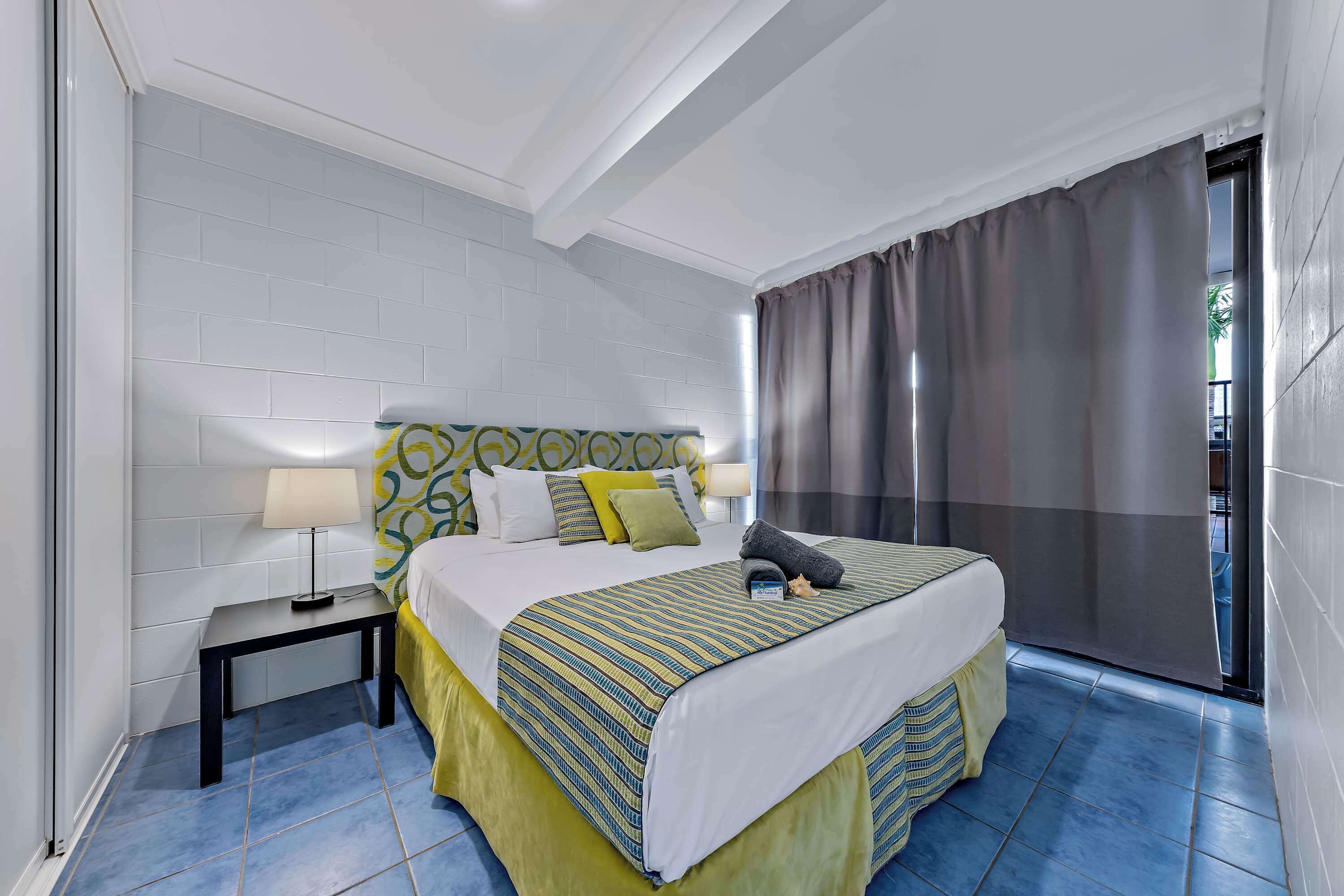 Quarto de hotel com uma cama, mesas de cabeceira e vista por uma cortina.