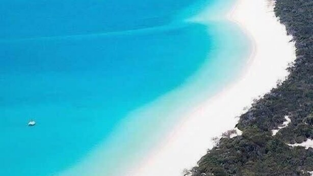 Un paysage côtier caractérisé par une mer bleue et limpide, une plage de sable et une végétation luxuriante.