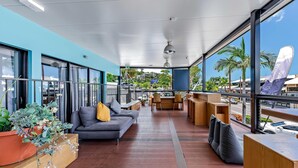 Un balcon spacieux avec un canapé gris, des tables en bois et des plantes en pot.