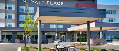 A modern hotel entrance with a covered parking area and a motorcycle parked in front.