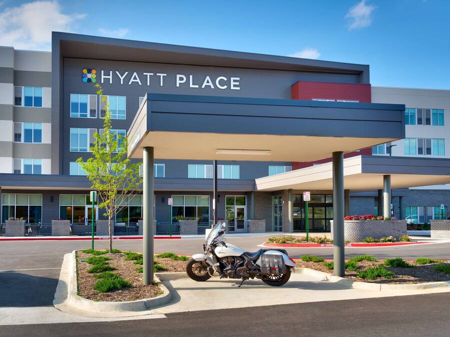 A modern hotel entrance with a covered parking area and a motorcycle parked in front.