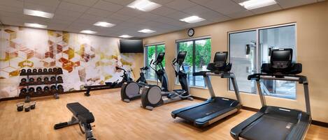 Un gimnasio con cintas de correr, elípticas y un banco.