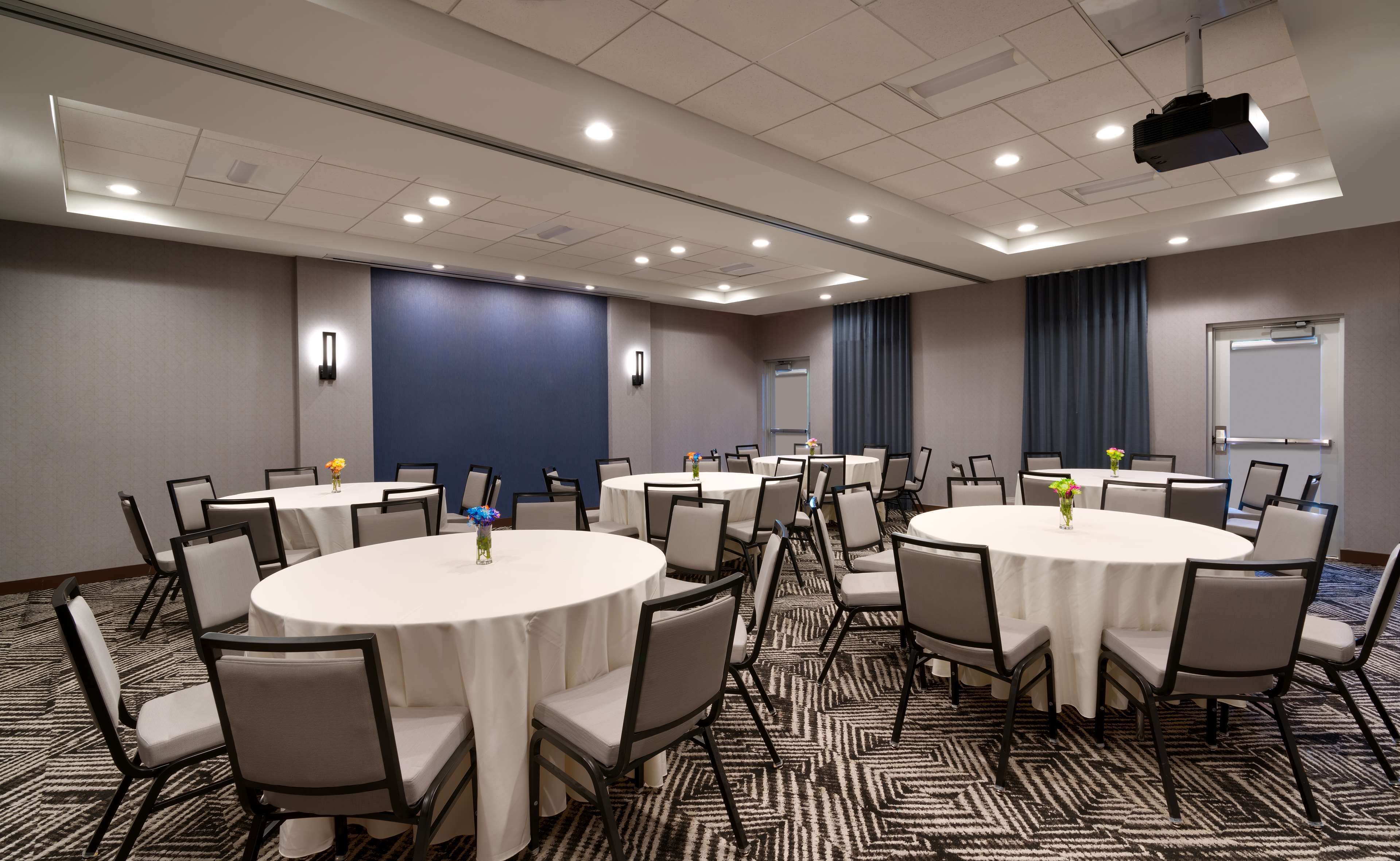 Un salón de conferencias con varias mesas redondas, sillas y una pantalla para proyector.