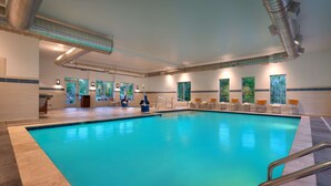An indoor swimming pool with clear blue water, surrounded by lounge chairs and a poolside area with a view of trees. - Hyatt Place Fayetteville/Springdale (Fayetteville)