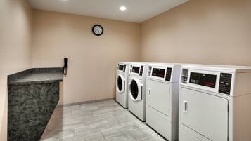 A laundry room with three front-loading washing machines, a clock on the wall, and a gray countertop.