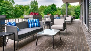 An outdoor patio with wicker furniture, a glass table, and brick flooring. - Hyatt Place Fayetteville/Springdale (Fayetteville)