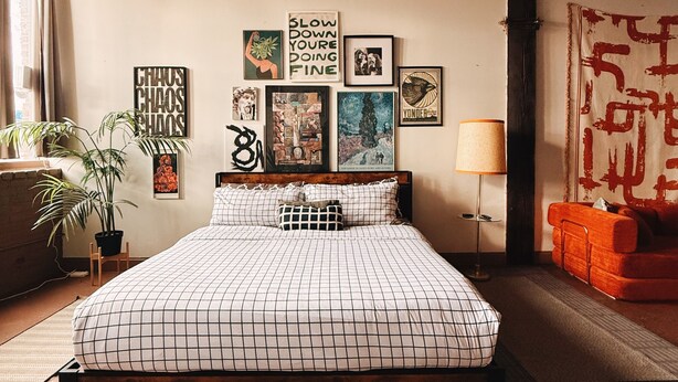 A bedroom with a wooden ceiling, a bed with a checkered bedspread, multiple framed artworks on the wall, a red sofa, and a floor lamp. - KING SUITE Loft Downtown 420 friendly - FREE PARKING - FREE Wifi (Detroit)