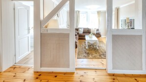 Une porte ouverte donne sur un salon où se trouvent un canapé, une table basse et un tapis.