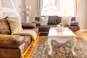 A brown leather sofa with cushions, a white coffee table with candles, and a vase with flowers.
