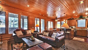 A log cabin interior with a living room, kitchen, and large windows.
