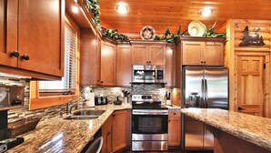 A modern kitchen with granite countertops, stainless steel appliances, wooden cabinets, and a decorative wreath on the ceiling.