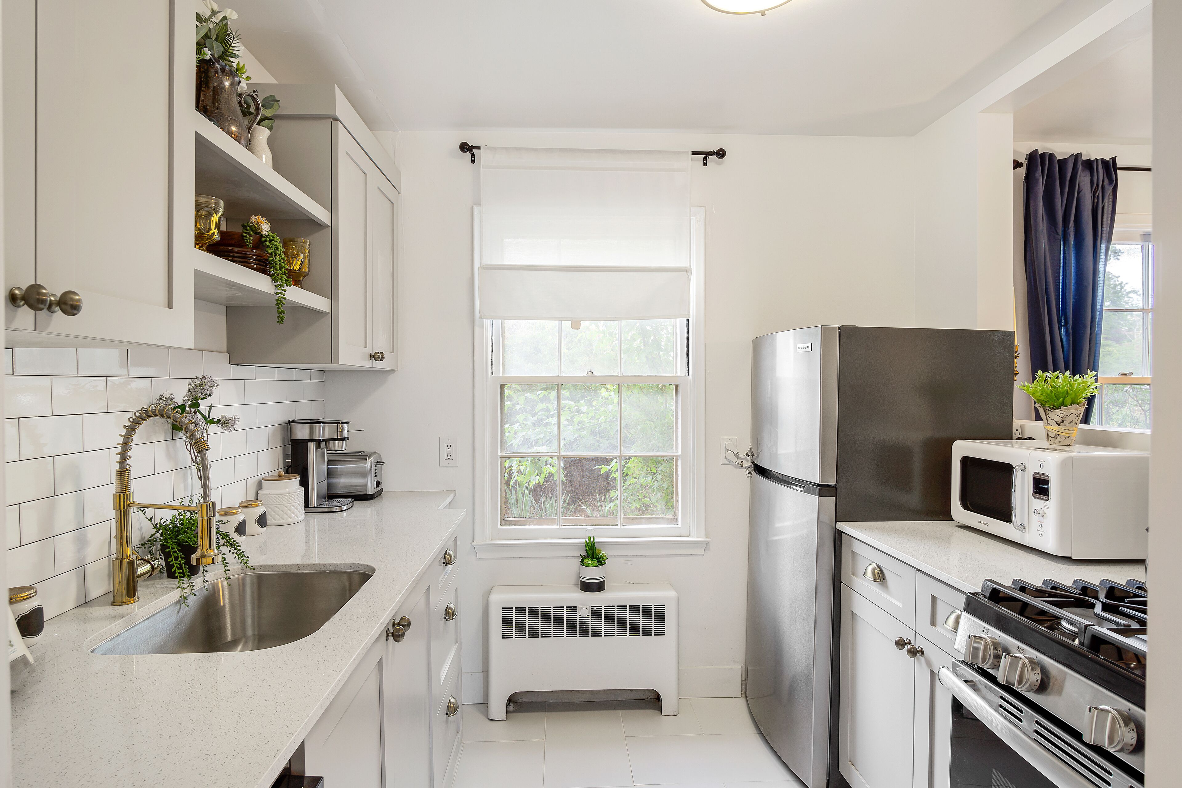 A modern kitchen with white cabinetry, stainless steel appliances, and a window with a white blind.