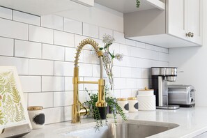 Una cocina con salpicadero de azulejos blancos, un grifo dorado, una cafetera y un tostador.