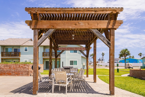 Una pérgola de madera con un letrero que indica 'No Smoking and Parking Permits Required' sobre un patio con mesas y sillas.