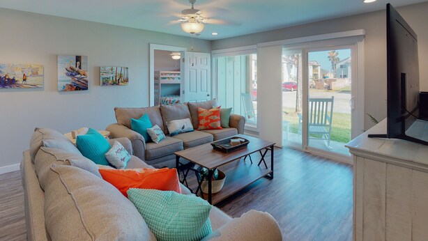 A spacious living room with a large sofa, a coffee table, and a television. There is a balcony with a view of the neighborhood. - 1st Floor, Shared Pool and Hot Tub, Near Marina and Ferry (Port Aransas)