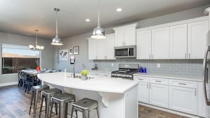 A modern kitchen with white cabinets, stainless steel appliances, and a central island with bar stools. - Southern Utah Vacationing at Its Best! (Hurricane)